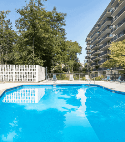 Sunny outdoor swimming pool beside apartment buildings and trees.